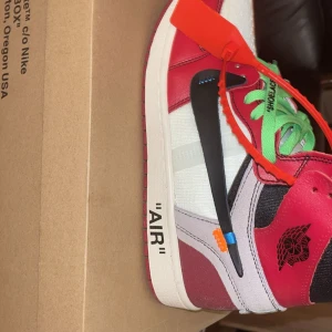 Nike Air Jordan 1 Off-White Chicago - Nike Air Jordan 1 Off-White Chicago med ikonisk röd, vit och svart färg, gröna skosnören och klassisk Off-White zip tie. Skon har tydliga detaljer som text på sidan, extra skosnören i olika färger och mix av skinn och textil. Perfekt för dig som vill sticka ut med en hypad sneaker. Endast seriösa köpare, inga byten!