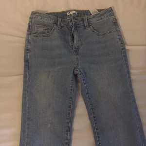 Ljusblå raka jeans - Säljer ett par ljusblå jeans med klassisk femficksdesign och raka ben. Jeansen har hög midja och är tillverkade i mjukt denimtyg som sitter snyggt på kroppen. Perfekta för dig som gillar en enkel och clean look.
