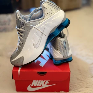 Nike sneakers silver och vit med blå sula - Nike sneakers i silver och vitt med snygga blå detaljer på sulan. Skorna har snörning, perforerade partier och en sportig design. Ovandelen är i syntet och mesh för bra andningsförmåga. Perfekta för dig som gillar en futuristisk look och vill sticka ut. de är nya