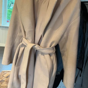 Ljusrosa kappa med bälte från H&M - Stilren ljusrosa kappa från H&M i storlek M. Kappan har ett bälte i midjan för snygg passform, klassisk krage och långa ärmar. Materialet är mjukt och känns lyxigt, perfekt för kyligare dagar. Enkel och clean look som passar till det mesta. 