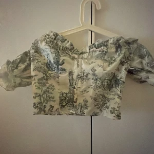 Offshoulder blus med grönt mönster SHEIN - Säljer en söt offshoulder blus från SHEIN i storlek XS. Blusen är vit med grönt, romantiskt mönster och har puffiga ärmar. Den är croppad och har en snygg, feminin passform som passar perfekt till jeans eller kjol.