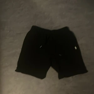 Svarta shorts från Polo Ralph Lauren - Svarta shorts från Polo Ralph Lauren med klassisk passform och dragsko i midjan. Diskret broderad logga på ena benet. Perfekta för en chill och sportig stil. Tillverkade i mjuk bomull för extra komfort.