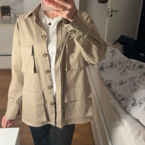 Beige jacka med fickor - Stilren beige jacka med fyra stora fickor framtill och knäppning med snygga knappar. Perfekt nu till hösten.