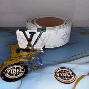 Lv  - Snyggt vitt bälte från Louis Vuitton med det ikoniska LV-spännet i silver. Bältet har diskret mönster och är gjort i skinn med en exklusiv känsla. Perfekt accessoar för att lyfta din outfit.