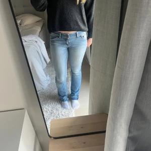 Ljusblå bootcut jeans - Snygga ljusblå jeans köpta på loppis med bootcut passform och låg midja. Jeansen har klassiska fem fickor, slitningar och broderade detaljer på bakfickorna. Tillverkade i mjukt denimtyg som sitter skönt och ger en avslappnad vibe.