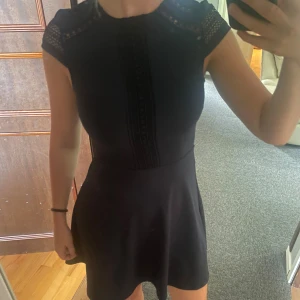 Marinblå klänning med spetsdetaljer - Supersnygg marinblå kort klänning med fina spetsdetaljer vid axlar och längs bröstet. Klänningen har en figurnära passform upptill och lätt utställd kjol. Perfekt för dig som gillar stilrena och eleganta plagg med en twist. Använd 1 gång. Stretchig material så passar alla från XS-M