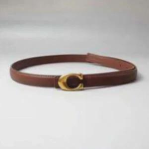 Brunt skärp med gulddetalj - Snyggt brunt bälte i skinn med en ikonisk guldfärgad C-spänne framtill. Perfekt accessoar för att lyfta din outfit med en klassisk touch och exklusiv känsla.