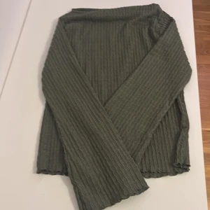 Olivgrön ribbad tröja från 157 - Olivgrön långärmad tröja från 157 med vågigt ribbat mönster. Tröjan har en enkel, rak passform och är tillverkad i ett mjukt, stretchigt material som känns skönt mot huden. Perfekt för lager-på-lager och chill dagar.