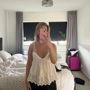 Vit broderad linnetopp med spetskant - Supersöt vit linnetopp med tunna axelband, v-ringning och broderade detaljer längst ner. Toppen har en luftig passform och spetskant som ger en romantisk vibe. Perfekt för varma dagar och enkel att styla med jeans eller kjol.