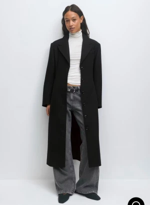 Figursydd kappa  - Stilren svart lång kappa med klassisk krage och knäppning framtill. Kappan har markerade axlar, raka ärmar och en snygg detalj med knapp i ryggen. Kappan är från Gina Tricot och är använd enbart vid ett tillfälle! 