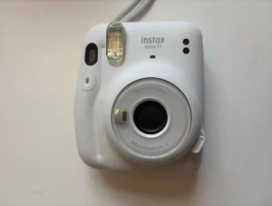 Instax Mini 11 - Polaroid kamera - Fujifilm Instax Mini 11 i vitt utförande. Enkel och rolig direktfilmskamera med inbyggd blixt och 60mm lins. Kameran i gott skick med minimalt slitage, perfekt för att ta omedelbara bilder och dela med vänner.