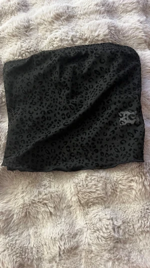 Svart leopardmönstrad tubtopp - Säljer en svart tubtopp med leopardmönster. Toppen är bandeau-modell och har en stilren, mörk look som passar perfekt till att skapa en edgy outfit. Materialet känns mjukt och följsamt mot huden. Perfekt för dig som gillar djurmönster och vill sticka ut.