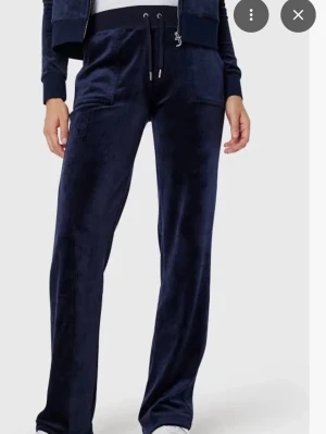 Mörkblå juciy couture - Snygga mörkblå mjukisbyxor i mjuk sammet med raka ben och snörning i midjan. Perfekta för chill dagar och har praktiska fickor framtill. Passar dig som gillar bekväma och stilrena plagg med lite extra lyxig känsla.