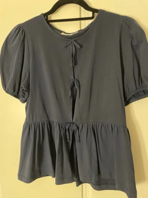 Mörkblå blus  - Säljer en mörkblå blus med tre dekorativa knyt framtill. Blusen har rund hals och volang nedtill som ger en söt och avslappnad look. Aldrig använt!! ❤️