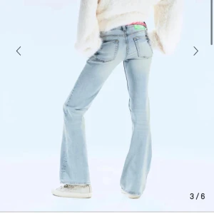 Ljusblå bootcut jeans med slitningar - Säljer ett par ljusblå bootcut jeans med snyggt slitna detaljer och klassisk femficksdesign. Jeansen har låg midja och är tillverkade i mjukt denimtyg. Perfekta för dig som gillar en retro vibe och vill sticka ut med en cool siluett.