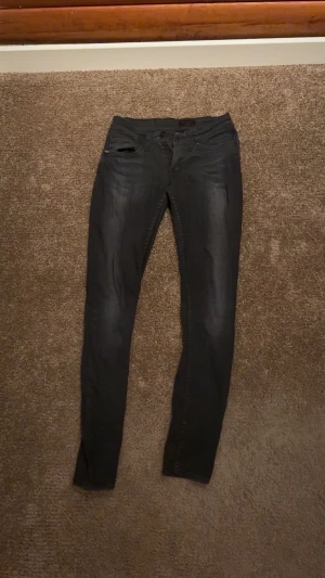 Svarta Tiger Of Sweden  jeans med smal passform  - Säljer ett par svarta  jeans från Tos med smal passform och klassisk femficksdesign. Jeansen har låg midja och är tillverkade i stretchigt jeansmaterial för en bekväm känsla. Vid frågor och funderingar, hör av dig.