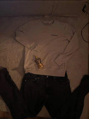 Beige långärmad tröja från Burberry - Säljer en beige långärmad tröja från Burberry med svart logotyp på bröstet och tryck med adress och koordinater på ryggen. Tröjan är storlek L och i ett väldigt bra skick. Den har tvättats en del gånger men är fortfarande bra i storleken och trycket sitter bra. 