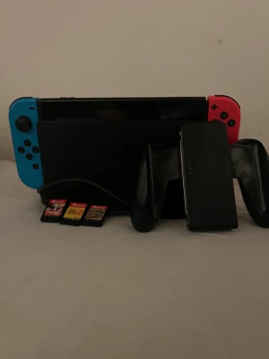 Nintendo Switch med spel och tillbehör - Nintendo Switch med blå och röd Joy-Con, dockningsstation, handkontrollshållare samt tre spel: 1-2-Switch, Minecraft och Super Mario Maker 2. Allt ser ut att vara i gott skick utan synliga skador eller slitage.den blåa kontrollen har stickdrift så man behöver byta ut den och inkluderat alla spel så runt 2500kr blir bra 😊 