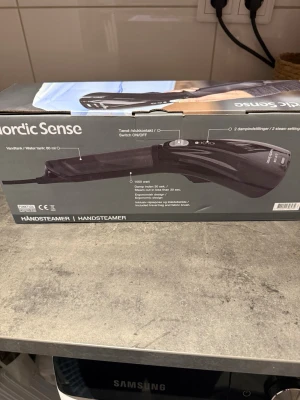 Handsteamer - Nordic Sense Handsteamer med 1000 watt effekt, 80 ml vattentank och ergonomisk design. Ånga på mindre än 30 sekunder, två ånginställningar och medföljande tygborste och resepåse. Produkten ser ut att vara i nyskick, förpackningen är hel och ren.