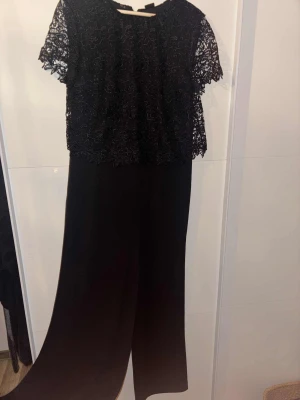 Svart långklänning med spets byxor till - Säljer en elegant svart långklänning med byxor till, överdelen har spets med tyg under. Den är i storlek 42 och använd en gång
