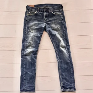 Dondup jeans  - Säljer ett par dondup jeans i blå tvätt med slitningar och snygga detaljer. Modellen har slim fit och klassisk femficksdesign. Jeansen har dragkedja och knappstängning. Jeansen har reparerats i skrevet tidigare men inget som syns, samt att stichingen på bakfickan har lossnat lite, Strl är 34 men passar som 32/32 ungefär