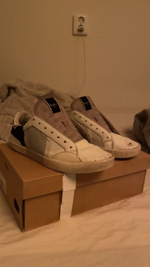 Pepe Jeans vita sneakers med svart detalj - Säljer ett par stilrena sneakers från Pepe Jeans i vitt med svarta detaljer på hälen och sidan. Skorna har rund tå, platt sula och snörningshål utan snören. Ovandelen är i skinn och mocka, med Pepe Jeans-logga på sidan och tungan. Perfekt för dig som gillar klassisk streetstil.