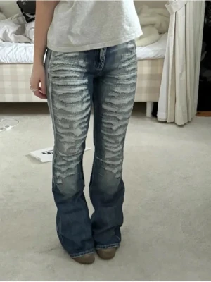 Lågmidjade bootcut jeans med slitningar  - Säljer ett par blå jeans med blekt tvätt och slitningar på framsidan. Perfekt för dig med unik och trenig stil. Storleken står inte nånstans men jag skulle säga att de passar dig som har xs-m. Skriv för fler frågor eller bilder