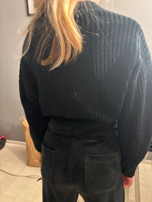 Svart ribbad kofta med stora knappar - Säljer en svart, croppad kofta med grov ribbad stickning och två stora, silvriga knappar framtill. Koftan har lång ärm och v-ringad hals. Perfekt för dig som gillar en chill och trendig look. Materialet är stickat och känns mjukt mot huden.