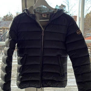 Mörkblå Colmar pufferjacka med huva - Säljer en snygg mörkblå pufferjacka från Colmar i storlek 42 (motsvarar 36 el xs). Jackan har huva, dragkedja framtill och två sidofickor. Insidan är ljusgrå och jackan har ett Colmar-märke på ärmen. En liten reva på höger axel är lagad med laglapp. Inga skador i övrigt. 