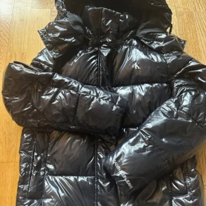 Svart pufferjacka från Calvin Klein Jeans - Snygg svart pufferjacka från Calvin Klein Jeans med glansig finish och logga på bröstet. Jackan har huva, dragkedja och är quiltad för extra värme. Perfekt för kalla dagar och har en modern, oversized look.