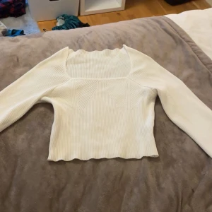 Vit ribbad långärmad topp - Säljer en vit ribbad topp med lång ärm och fyrkantig halsringning. Toppen har en croppad passform och vågig kant nedtill, samt snygga ribbade detaljer som ger extra stilpoäng. Perfekt för dig som gillar minimalistisk och fräsch look. Pris kan diskuteras och köparen står för frakt