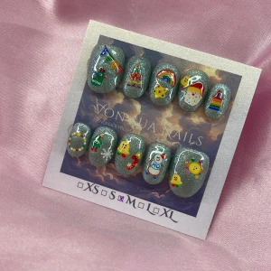GreenXmas(M);ExtraShortOval  - Set med handgjorda press-on naglar i silverglittrig bas, dekorerade med färgglada motiv som regnbåge, julgran, snögubbe, stjärna, tomte och söta figurer. Oval form och i storlek M: 16 mm, 12 mm, 12,5 mm, 11,5 mm, 10 mm. Perfekt för dig som vill ha roliga och unika naglar.