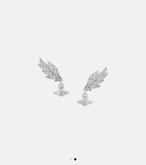 Vivienne Westwood örhängen med vingar - Supersnygga örhängen från Vivienne Westwood i silverfärg med ikoniska orb-symbolen och detaljerade vingar. Designen är glittrig och unik, perfekt för dig som gillar statement-smycken. Kommer med original ask och tygpåse. Dessa är helt slutsålda!