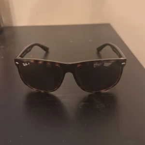 Ray-Ban Wayfarer brunmelerade solglasögon - Snygga Ray-Ban Wayfarer solglasögon med brunmelerad båge och svarta polariserade glas. Klassisk fyrkantig form med silverdetaljer vid bågens front. Modellen är RB4147 och passar dig som gillar tidlös stil med en touch av retro.