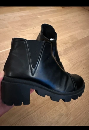Svarta chunky boots - Höst/ Vinter - Säljer ett par svarta boots med grov plattformsula och låg klack. Skorna har rund tå och är tillverkade i skinn med elastiska paneler på sidorna för enkel påtagning. Perfekt för dig som gillar en edgy och stilren look.