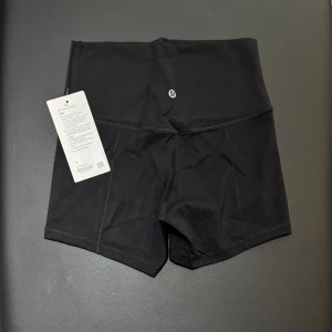 Svarta high Align waist shorts från Lululemon storlek 6 - Säljer ett par svarta, align högmidjade träningsshorts från Lululemon i mjukt och stretchigt Nulu-material. De har en clean look, korta ben och en dold ficka i midjan. Perfekta för gymmet eller yoga, med bekväm passform och snygg siluett.