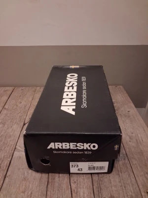 Arbesko svarta sneakers med blå detaljer - Svarta sneakers från Arbesko med ventilerande mesh och slitstarka partier i skinn och syntet. Snygga blå mönstrade remmar med kardborre för enkel justering. Robust platt sula med bra grepp och rund tå. Perfekt för dig som vill ha både funktion och stil.