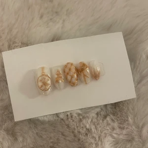 Glittriga lösnaglar i guld och vitt - Jag säljer dessa handgjorda press on naglarna med fina guld detaljer, perfekt till jul! Man får 10 stycken naglar och ett prepp paket för att få sån lång hållbarhet som möjligt. Med den rätta preppen så kan de hålla 4+ veckor, från mina egna erfarenheter. Ifall du är intresserad av ett annat sett eller andra storlekar så uppskattar jag verkligen att ni kontaktar mig! 