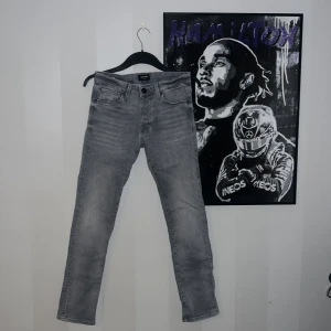 Grå slim jeans Jack & Jones Glenn - Snygga grå jeans från Jack & Jones i modellen Glenn. Slim fit med klassisk femficksdesign och diskret slitning vid bakfickan. Jeansen har en fräsch tvättad look och är tillverkade i mjukt bomullsmaterial med stretch för extra komfort. Har dock tyvärr ett hål på baksidan av byxorna men annars riktigt snygga