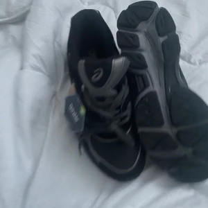 Svarta Asics sneakers strl 42 - Säljer ett par svarta Asics sneakers med grå detaljer. Oanvända skor. Pris kan diskuteras. 