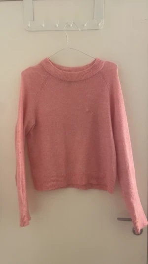 Rosa stickad tröja från Vero Moda - Mysig rosa stickad tröja från Vero Moda i storlek S. Tröjan har en rund halsringning, ribbade muddar vid ärmslut och nederkant samt långärmad passform. Perfekt för att hålla dig varm under kyliga dagar och har en mjuk känsla mot huden. Ett litet hål på tröjan som är ihopsytt men knappast så att de syns när man har på sig den.😊