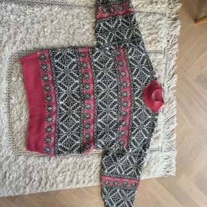 Vintage stickad tröja  från Lacoste - Säljer en äkta vintage stickad mohair tröja från Lacoste med svartvitt grafiskt mönster och breda rosa partier. Tröjan har krage i rosa, långa ärmar och klassisk Lacoste-logga på bröstet. Perfekt för dig som vill sticka ut med retrovibbar och ha en unik tröja i vinter! I jättebra skick. Strl 42 men passar både dig som har XS, S  och M beroende på hur du vill att den sitter 