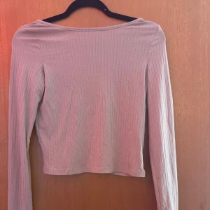 tröja med öppen rygg - Säljer en ljusbeige croppad topp med lång ärm och djup, rundad rygg. Toppen är ribbad och har en tight passform som framhäver siluetten. Perfekt för att styla med höga jeans eller kjol.