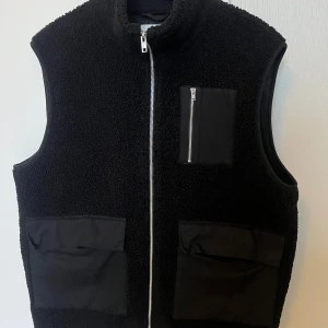 Svart fleeceväst från Ciszere - Svart fleeceväst från Ciszere med hög krage och silverfärgad dragkedja framtill. Västen har två stora fickor nedtill och en mindre bröstficka med dragkedja. Perfekt för lager-på-lager och chill stil.  Bra skick och storlek L