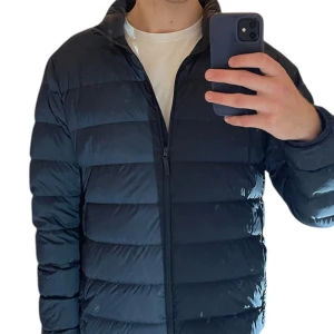 Svart dunjacka från Uniqlo L - Säljer en svart Ultra Light Down dunjacka från Uniqlo i storlek L. Jackan har en stilren, quiltad design med dragkedja framtill och långärmade ärmar. Perfekt för dig som vill ha en lätt och varm jacka med clean look.