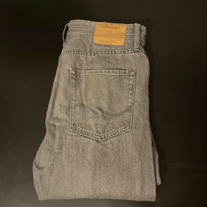 Grå jeans från Jack & Jones, 30/30 - Snygga grå jeans från Jack & Jones i klassisk straight fit. Jeansen har fem fickor, en läderpatch med logga bak och är tillverkade i slitstarkt denim. Passar dig med storlek 30/30.