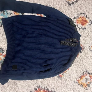 Marinblå ribbad tröja från Guess - Snygg marinblå ribbad tröja från Guess med lång ärm och coola svarta detaljer vid axlarna och halsen. Tröjan har knappar vid halsen och är tillverkad i mjukt stickat material. Perfekt för dig som gillar stilrena och moderna plagg. Bra för grisch stil med en tröja inte många har . Storlek xs men passar storlek s. Knappast använd