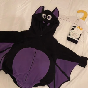 Svart och lila fladdermus  - designad som en fladdermus med stora ögon på huvan, lila detaljer på magen, öronen och vingarna. Tröjan har dragkedja framtill och är gjord i mjuk fleece, perfekt för höst och vinter. Huvan har öron och ansikte för extra gullig look.