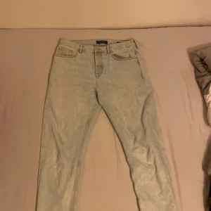 Jeans från Scotch & Soda - Säljer ett par ljusblå jeans från Scotch & Soda med klassisk femficksdesign och snygga blå X-detaljer på bakfickan. Jeansen har rak passform och är tillverkade i mjukt denimtyg. 