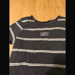 Randig svart t-shirt från Levis - Svart t-shirt från Levis med vita horisontella ränder och broderad logga på bröstet. Klassisk rund hals och korta ärmar. Tillverkad i mjuk bomull, perfekt för en avslappnad stil.